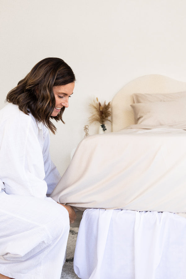 women happily tucking in the top sheet of a beautiful beige bedding set