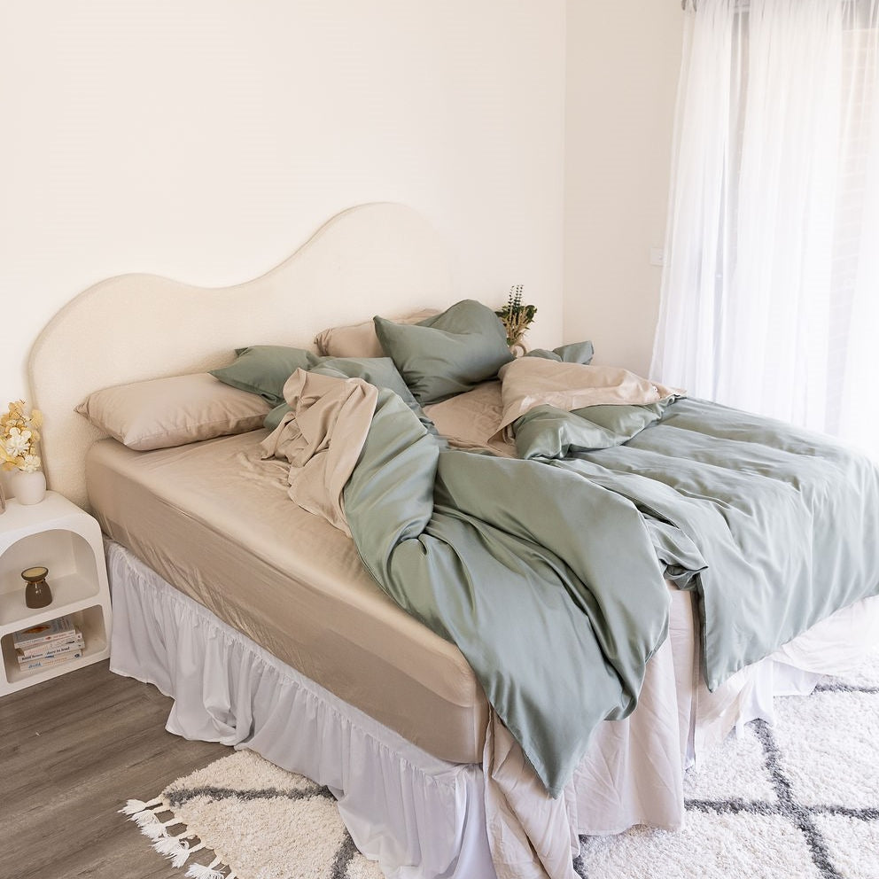 Messy bed with beige sheets and eucalyptus green quilt cover