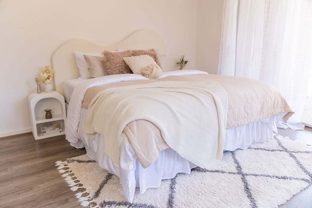 aesthetically styled bed with white sheets and beige quilt covers, styled with coverlet, throw and decorative pillows