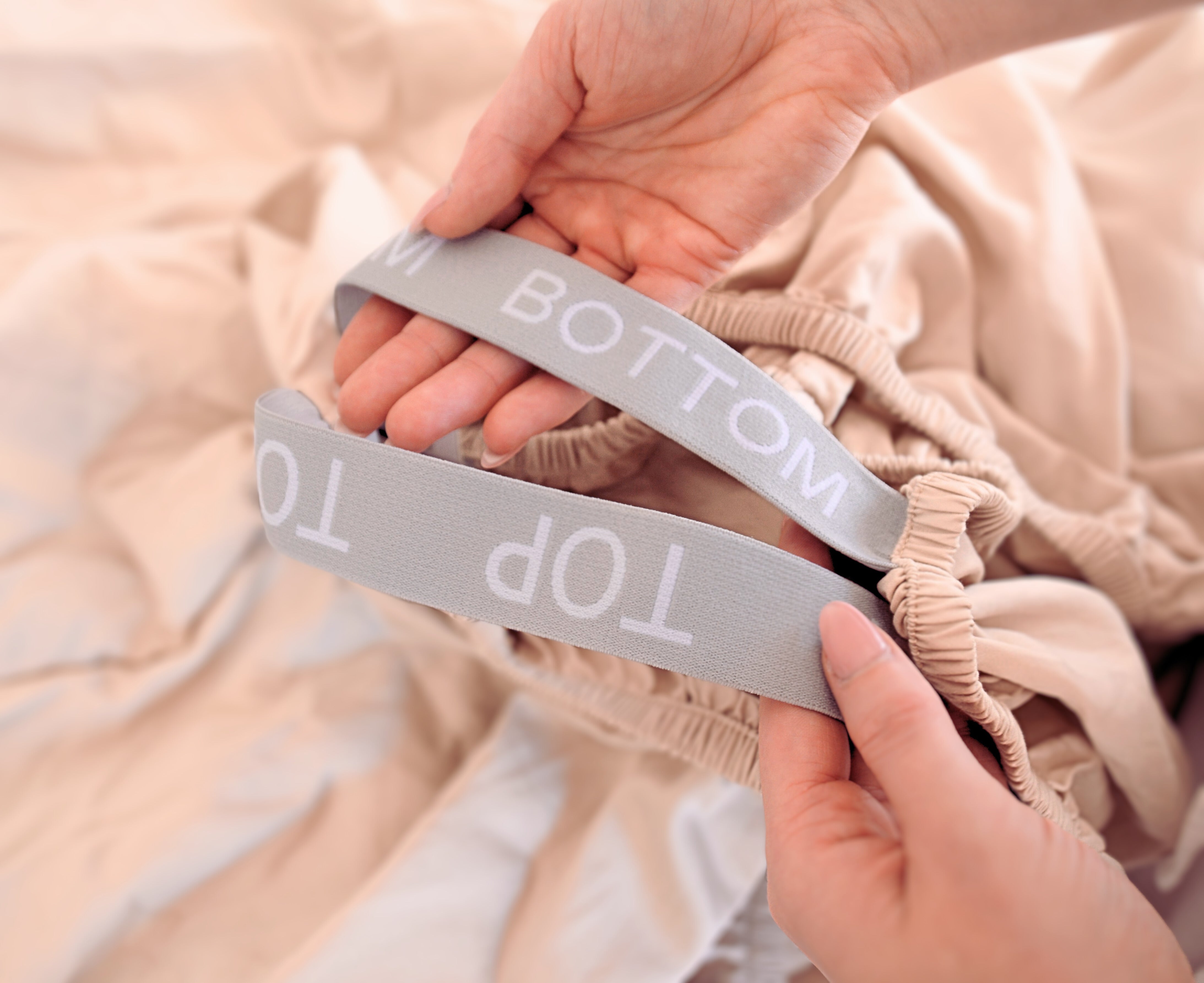 fitted sheet corner straps showing elastic labelled with TOP and BOTTOM, help by female hands