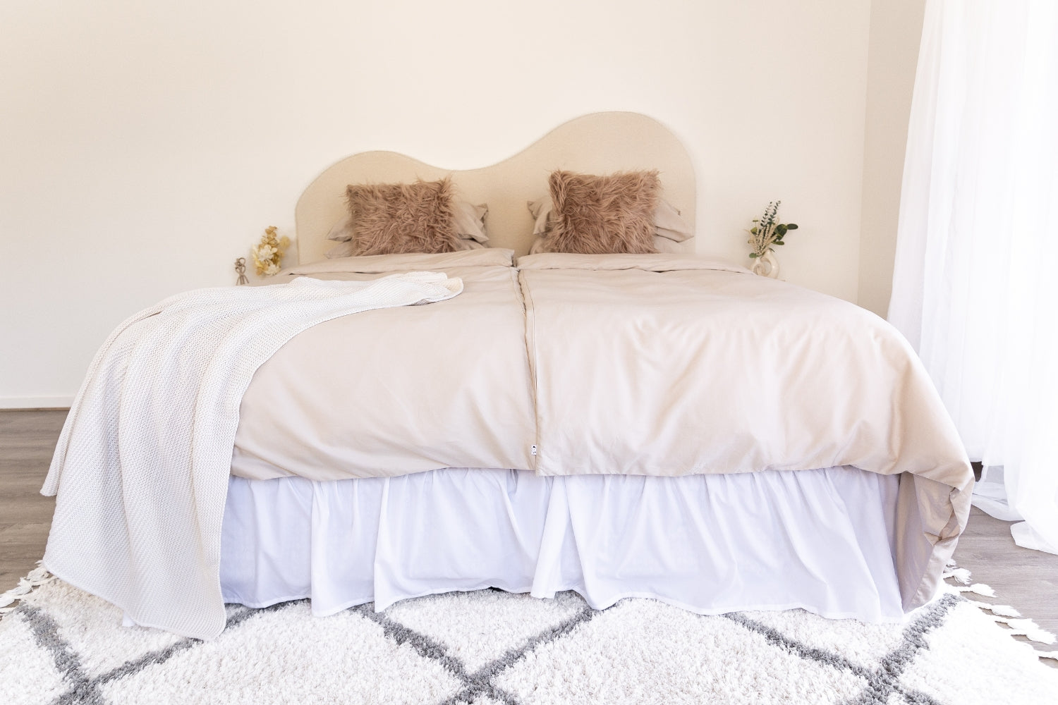 Neatly made bed with 2 beige single quilt covers and a cream throw with decorative pillows in a bedroom setting.