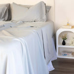 Close up of King/Queen bamboo cotton sheet set in grey sage styled on bed with nice side table