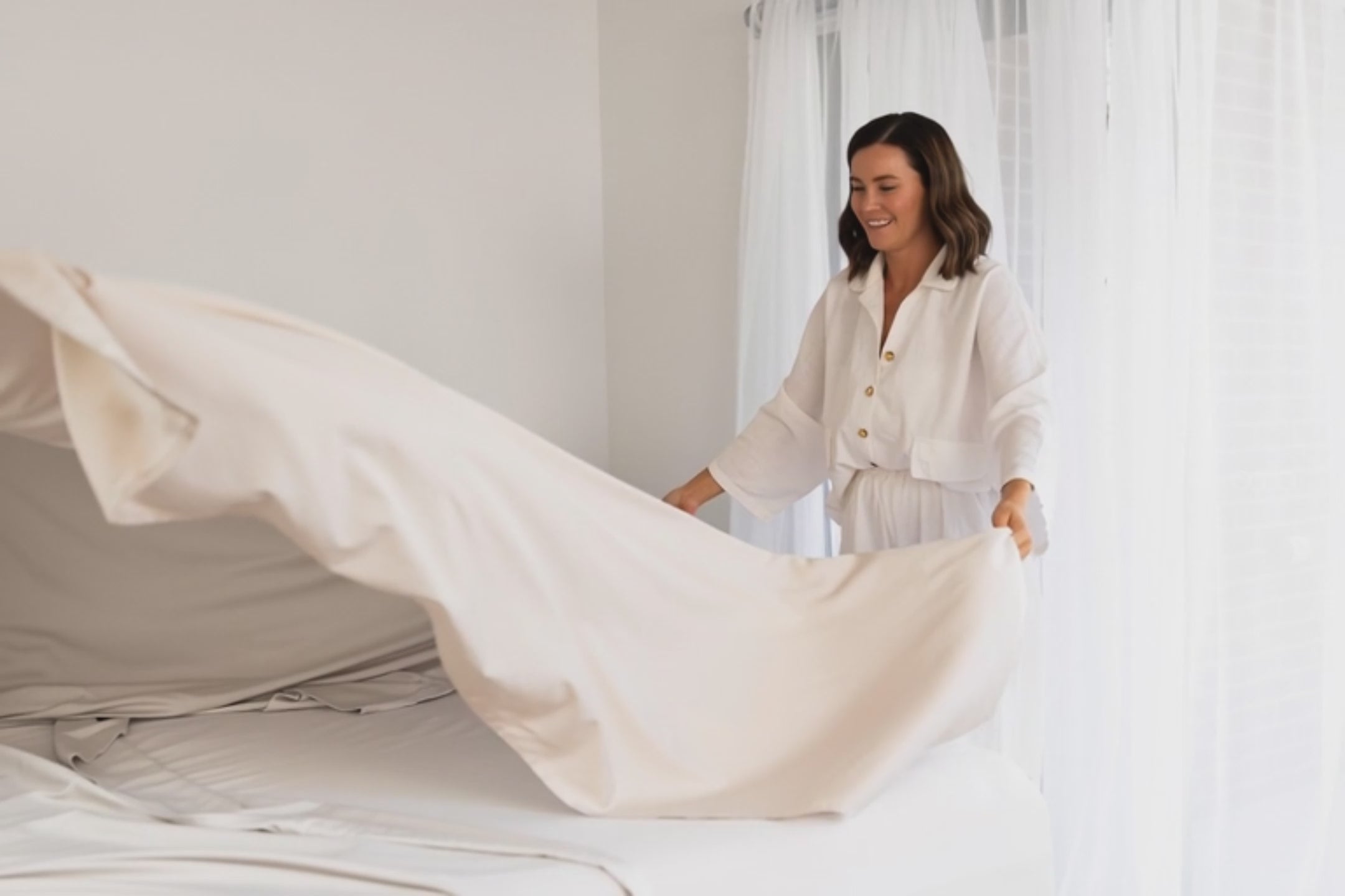 short video of women smiling while placing a beige sheet on a bed