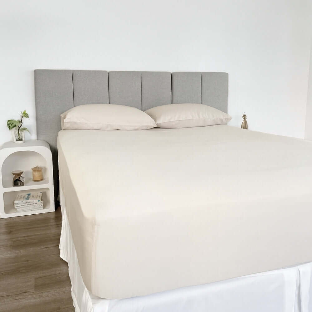 corner view of bed styles with beige fitted sheet and 2 matching pillows with grey headboard