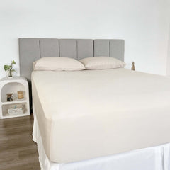 corner view of bed styles with beige fitted sheet and 2 matching pillows with grey headboard