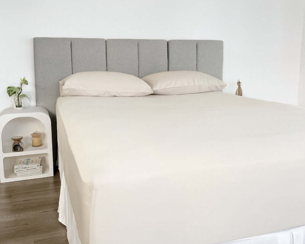 corner view of bed styles with beige fitted sheet and 2 matching pillows with grey headboard