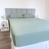corner view of bed styles with eucalyptus green fitted sheet and 2 matching pillows with grey headboard