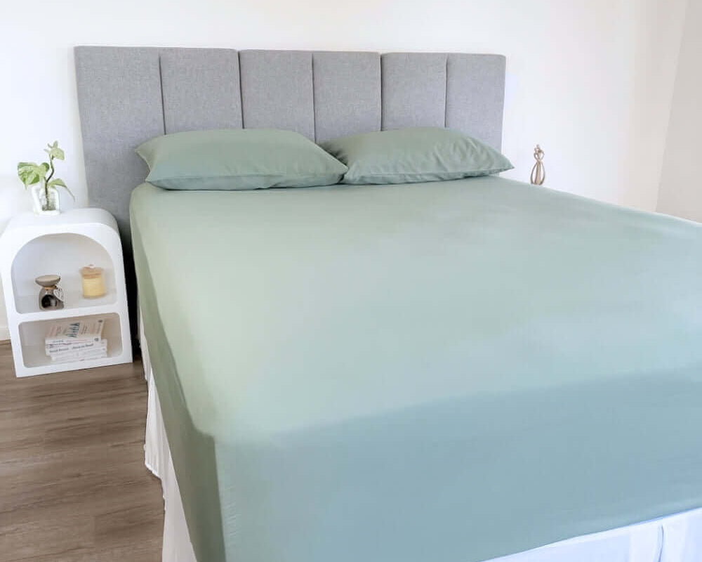 corner view of bed styles with eucalyptus green fitted sheet and 2 matching pillows with grey headboard