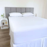 corner view of bed styles with white fitted sheet and 2 matching pillows with grey headboard