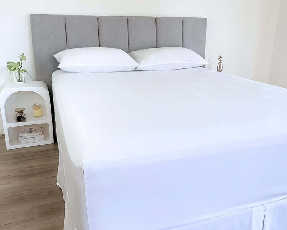 corner view of bed styles with white fitted sheet and 2 matching pillows with grey headboard