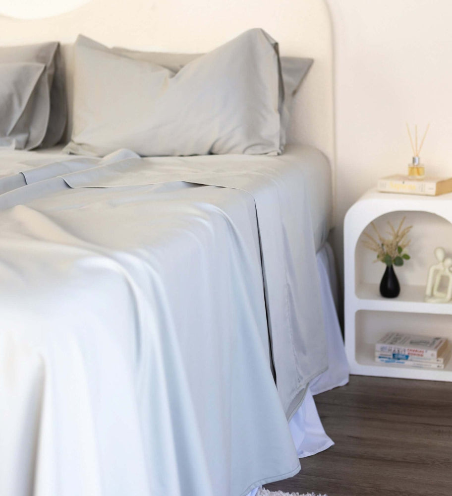Close up of King/Queen bamboo cotton sheet set in grey sage styled on bed with nice side table